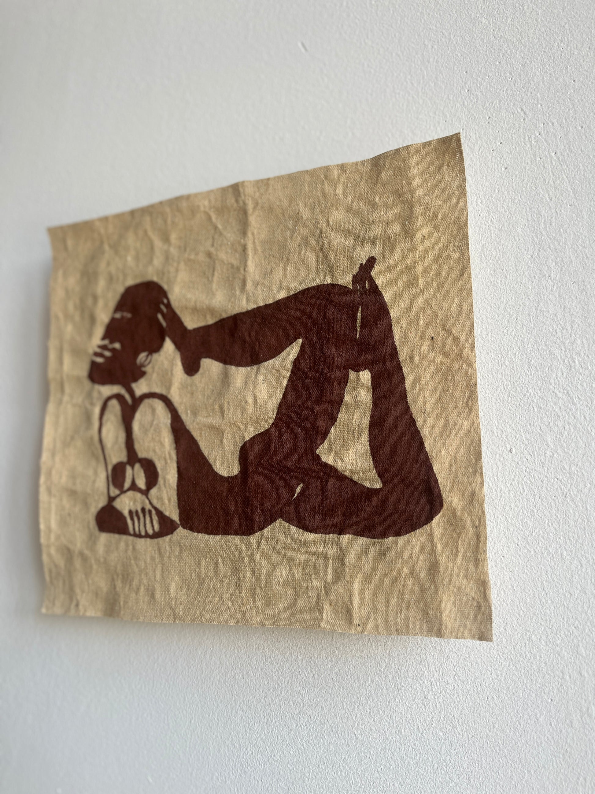 Silhouette of a person in a yoga pose on a brown textile against a white wall.