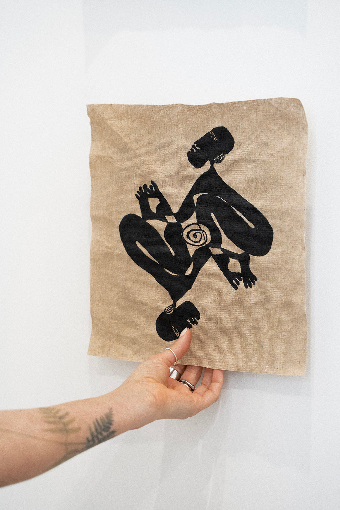 Hand holding a beige raw canvas with black silhouette design against a white background