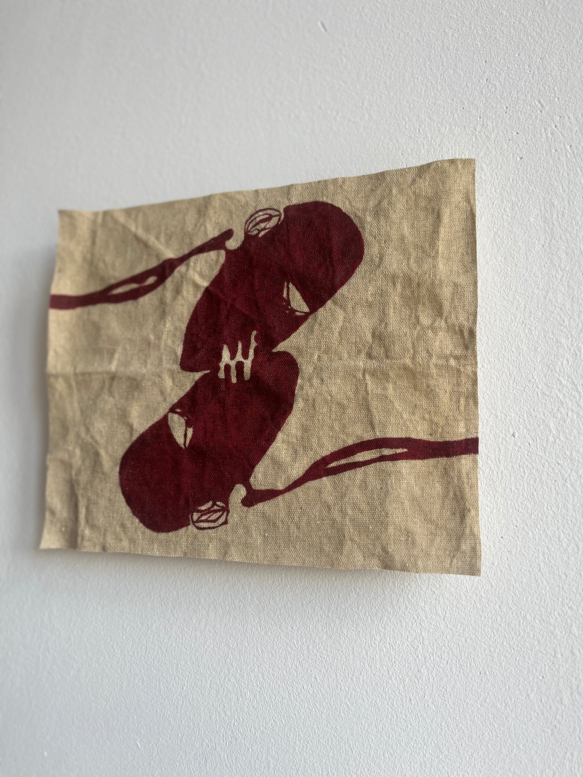 Artistic depiction of two figures kissing on crumpled raw canvas against a white wall.