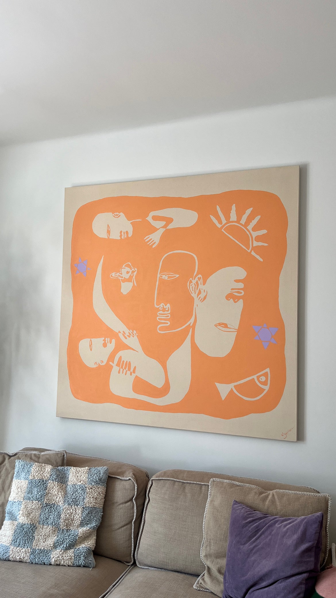 Decorative wall art with abstract designs on a beige background, hanging above a sofa with patterned cushions.